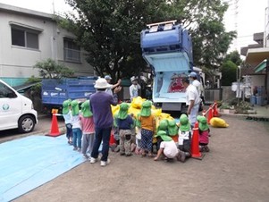 写真：ごみが積み込まれていく様子が観察できる清掃車「ごみぱっくん号」の説明をする清掃職員と、説明を聴く園児